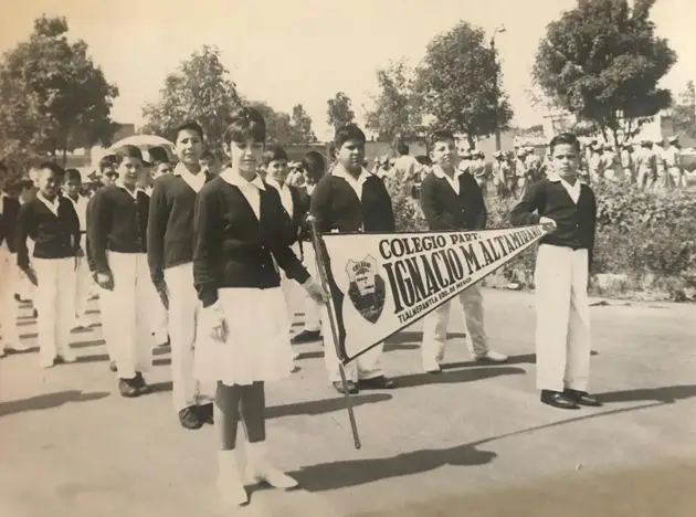 Dos niños marchando con el banderín del colegio durante una celebración escolar.