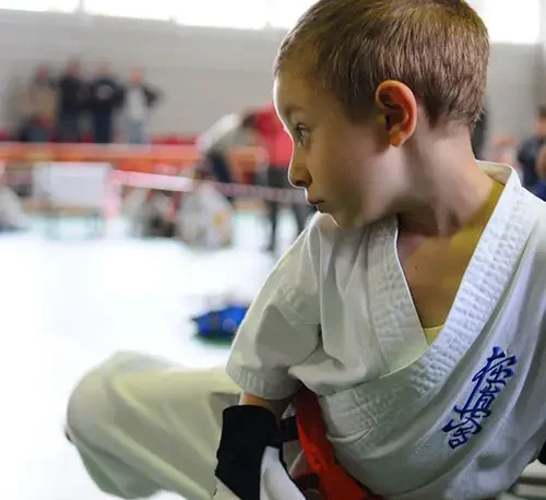 Niño con traje de karateca entrenando con un costal de Taekwondo.