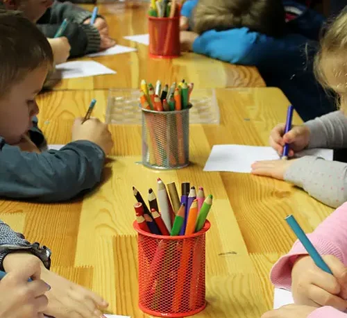 Niños haciendo tareas con lápices de colores y cuadernos en el Club de Tareas.